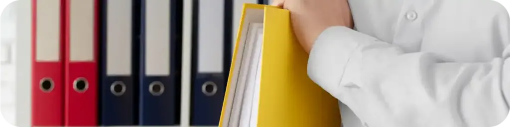 Kantoormedewerker met mappen en documenten bij archiefkasten, wat staat voor georganiseerd documentbeheer.