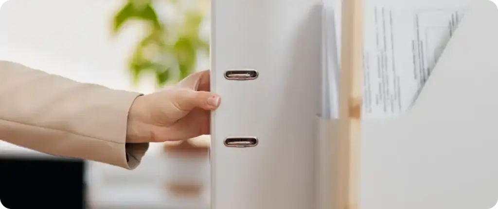 Met de hand een ordner uit een kantoorkast halen, ter illustratie van het opzoeken van documenten en het overzichtelijk opbergen van dossiers.