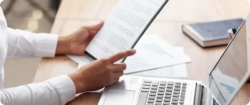 Zakelijke professional die documenten op een laptop bekijkt, waarmee de productiviteit op kantoor en documentanalyse worden benadrukt.