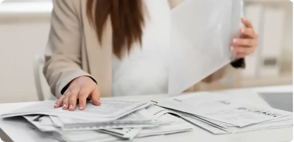 Kantoormedewerker die een grote stapel documenten doorneemt, wat staat voor administratieve taken en het verwerken van papierwerk.