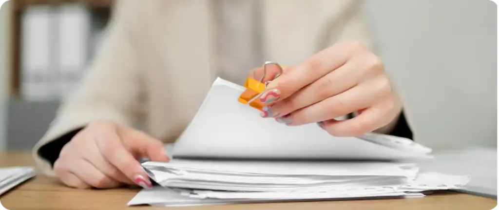 Handen die papierwerk sorteren met behulp van een bindclip op een bureau, waarmee de organisatie van documenten en de workflow worden getoond.