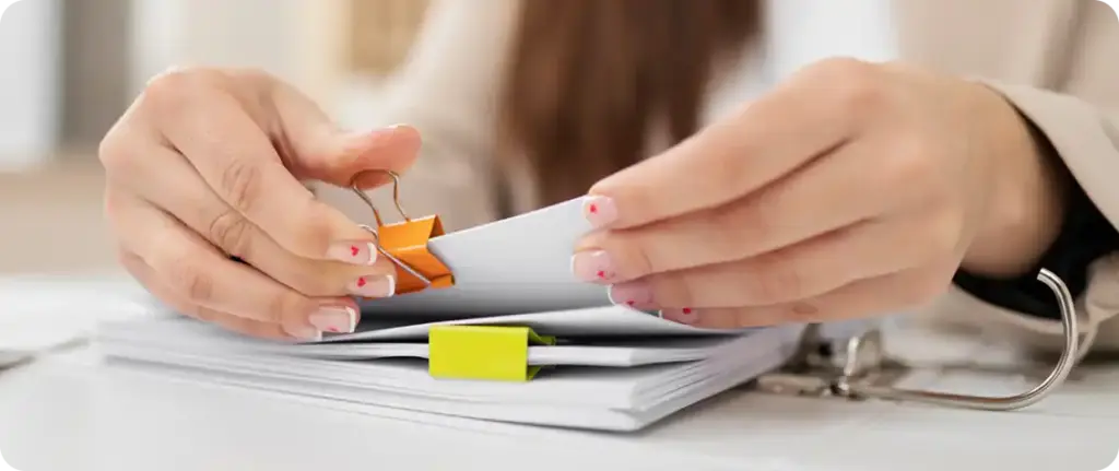 Handen die op een bureau op papierwerk stempelen, wat staat voor goedkeuring van documenten, verificatie en administratieve workflow.